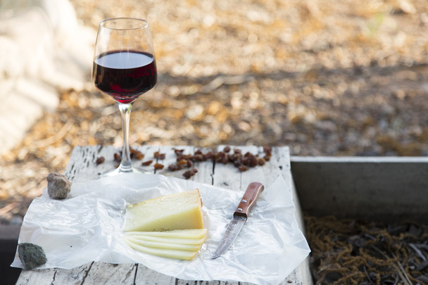 Kawałki sera i rodzynki z kieliszkiem wina czerwone na płycie starego drewna - Zdjęcie, obraz