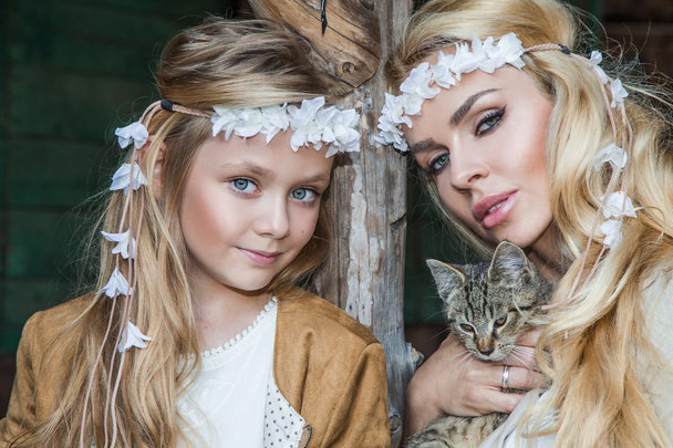eine schöne blonde Frau mit einem kleinen Mädchen, das sich im Wilden Westen kuschelt, in weißen Kostümen mit einer Katze an den Händen - Foto, Bild