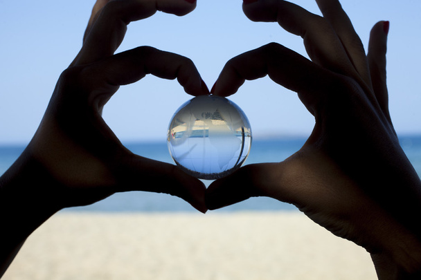 Globo de cristal em mãos humanas mostrando gesto de forma de coração
 - Foto, Imagem