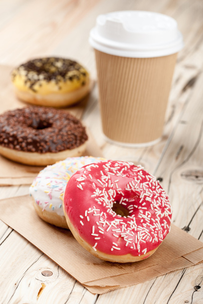 Colorful donuts and paper cup on wooden table - Photo, image