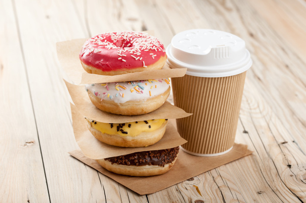 Colorful donuts and paper cup on wooden table - Foto, Imagem