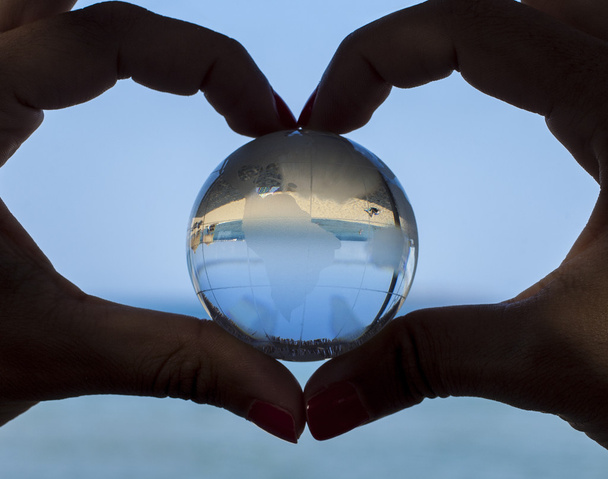 Globo de cristal em mãos humanas mostrando gesto de forma de coração
 - Foto, Imagem