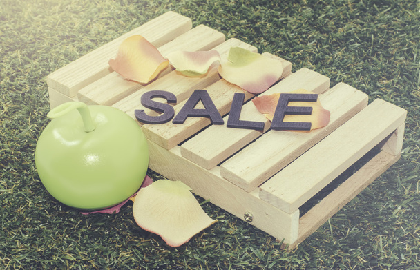 Image concept word sale on pallet, apple light with artificial petal and grass. Grain and faded retro vantage look background - Photo, Image