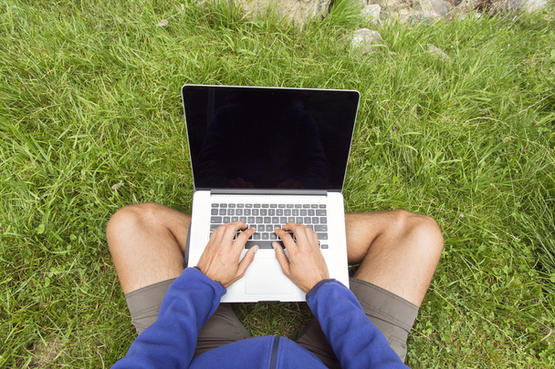 Чоловік працює в природі на ноутбуці над зеленою травою
 - Фото, зображення