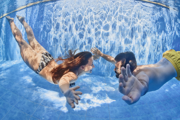 Positive couple swimming underwater in outdoor pool - Foto, afbeelding