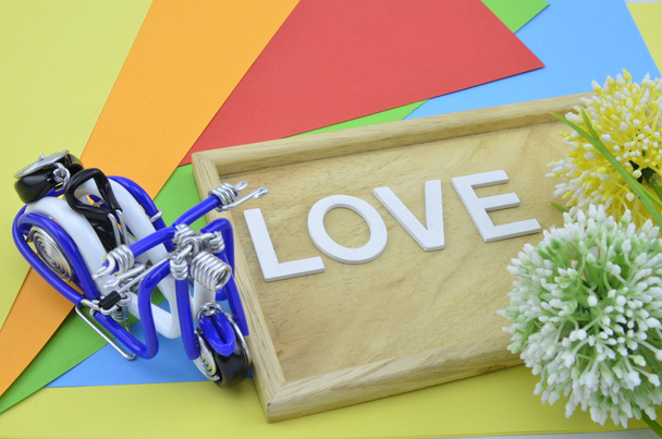palavra branca e símbolo de amor preto em colourfull background.green, amarelo e flor artificial branco colocado à direita. mini scooter azul colocado à esquerda
 - Foto, Imagem