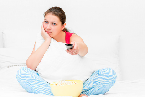 dissatisfied girl in pajamas with a TV remote control - Foto, imagen