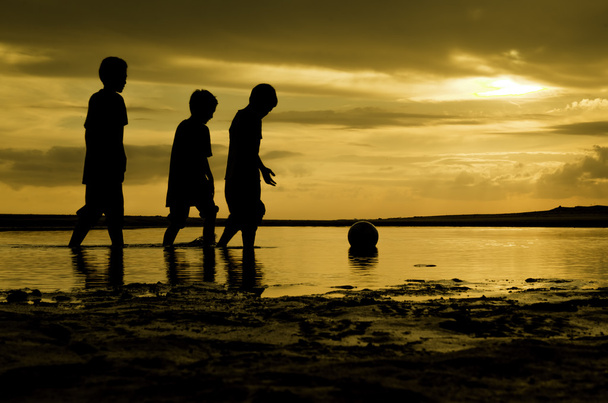 水の上をボールに向かって歩いてシルエット 3 人の少年をイメージします。日没日の出と水に反射 - 写真・画像