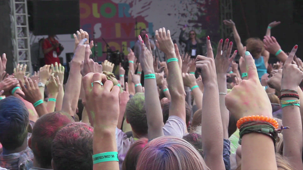 Man throwing paint powder in crowd from stage, people enjoying fest, hands up - Footage, Video