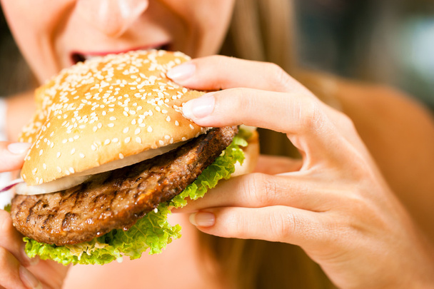 Woman in a restaurant eating hamburger - Photo, Image