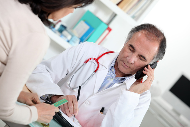 Doctor talking on the phone during a consultation - Φωτογραφία, εικόνα