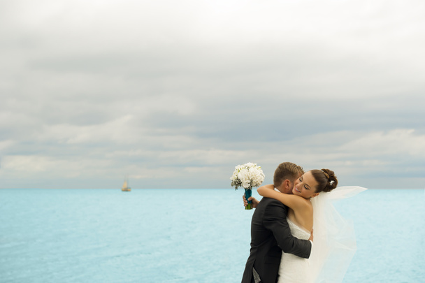 The groom is holding her bride on the sea background. - Photo, Image