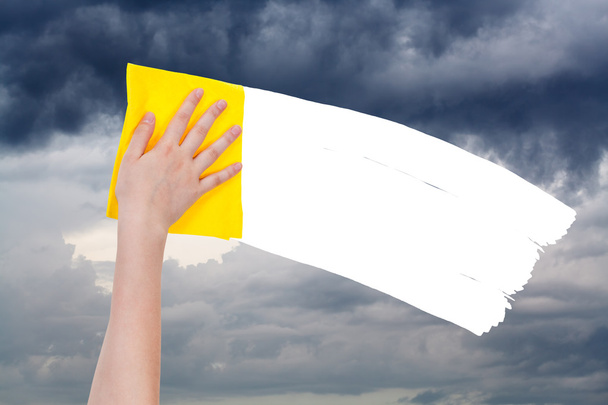 Рука удаляет пасмурное небо желтой тряпкой
 - Фото, изображение