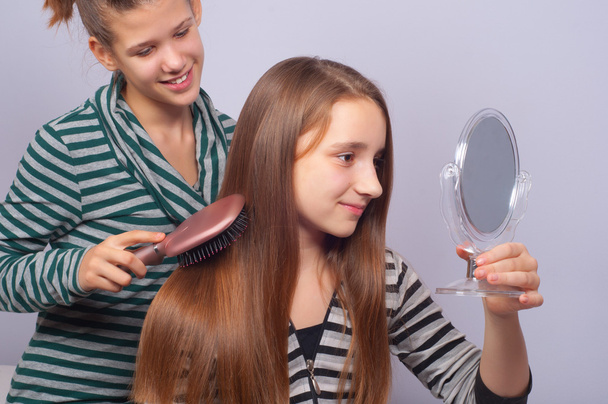 Pretty teenage girls combing hair and watching themselves in mirror - Photo, Image