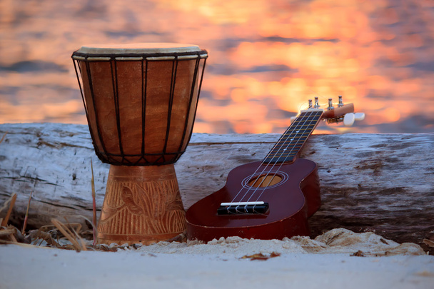Ukulele e tambor étnico sobre uma praia de pôr do sol
. - Foto, Imagem