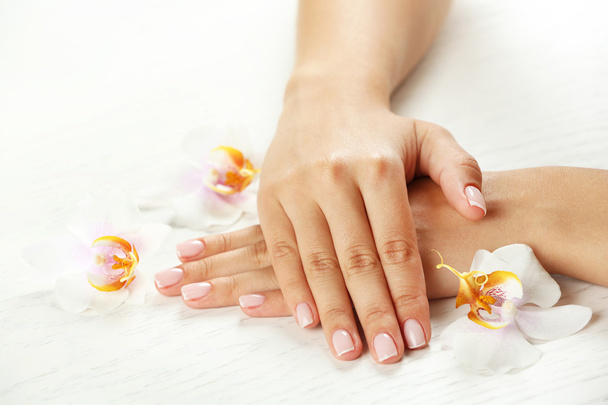 Woman hands with french manicure and orchid flowers on wooden table close-up - Foto, afbeelding