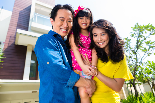 Азиатская семья с ребенком, стоящая перед домом
 - Фото, изображение