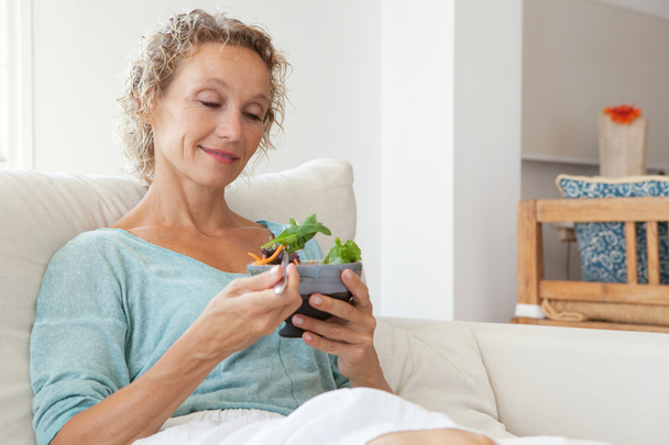 mujer comiendo una ensalada en un sofá en casa
 - Foto, Imagen