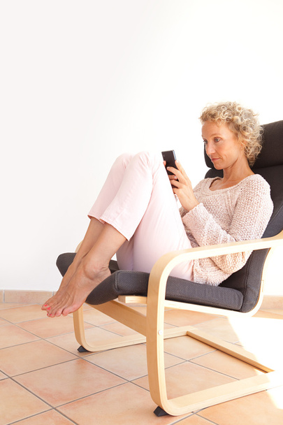 woman in an armchair using a smartphone - Fotoğraf, Görsel