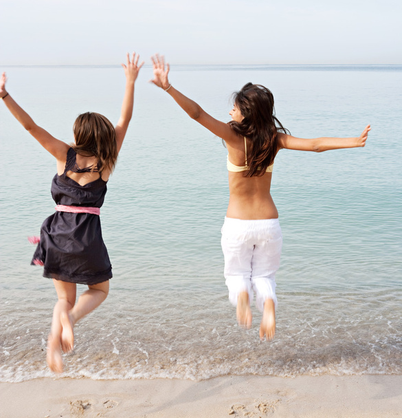 girls jumping up in the air together on beach - Photo, Image