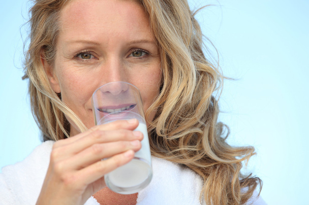 Closeup of woman in bathrobe drinking a glass of milk - Zdjęcie, obraz