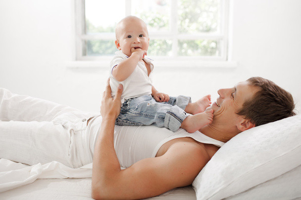 young father with his nine months old son on the bed at home - Фото, изображение