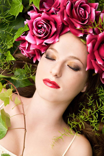 woman laying in a forest wearing a red roses head dress - Foto, afbeelding