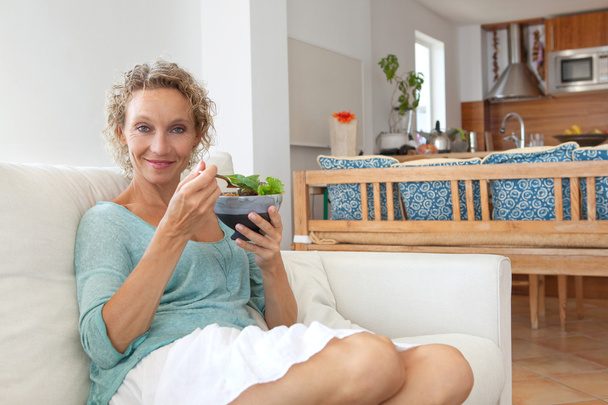 woman eating a salad on a couch at home - Photo, Image
