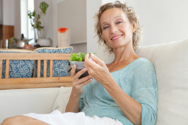 woman eating a salad on a couch at home - Foto, afbeelding