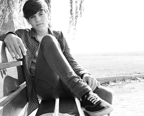 boy sitting on a wooden bench in a park - Zdjęcie, obraz