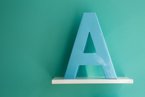 Letter A turquoise color on a white shelf. - Фото, зображення