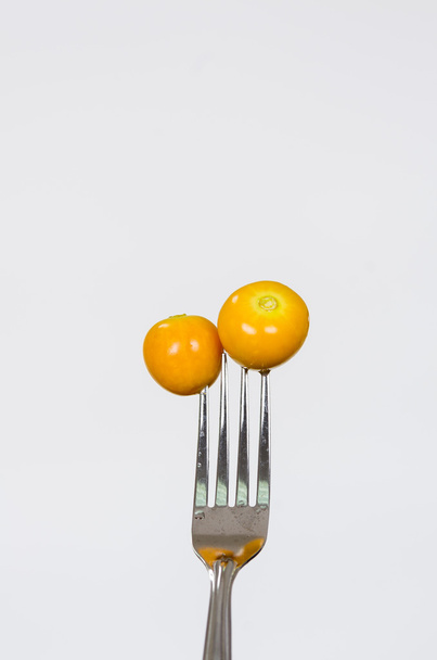 Closeup silver fork with two delicious orange gooseberries and white background - 写真・画像