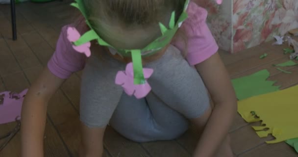 Kislány a Pink póló szőke Braid ül a padlón, hogy egy alak színes papír, ül egy zöld korona, gyerekes könyv - Felvétel, videó
