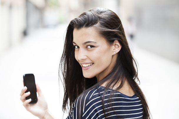 Happy woman using a smart phone in the street with an unfocused background - Foto, Imagem