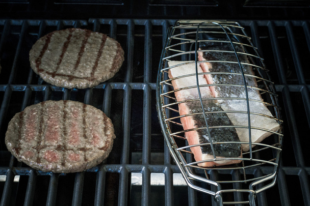 Two hamburger slices and salmon steak on grill rack - Photo, Image