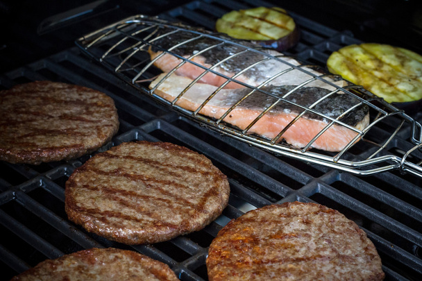 Hamburger slices, salmon steak and eggplant on grill rack - Photo, Image