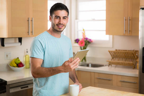 Homme avec tablette intelligente dispositif de lecture des nouvelles du matin avec une tasse de café à la maison mâle célibataire
 - Photo, image