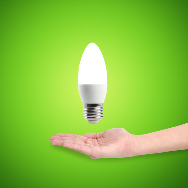 Glowing LED energy saving bulb in a hand on a green background - Photo, Image