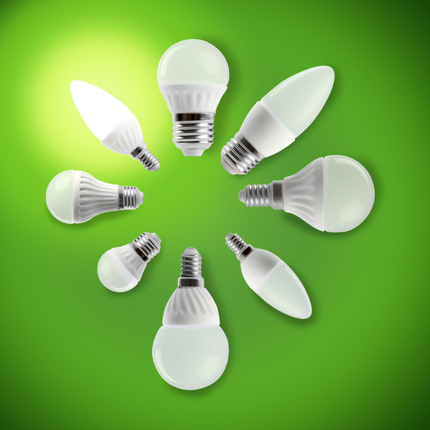Ampoule LED à économie d'énergie lumineuse dans une main sur un fond vert
 - Photo, image