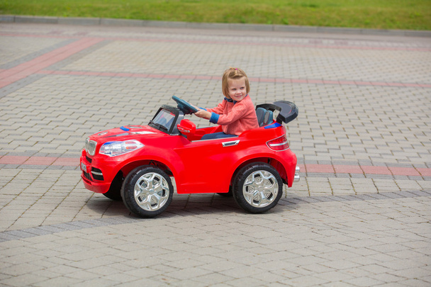 Beautiful little girl riding toy car in summer park - Foto, imagen