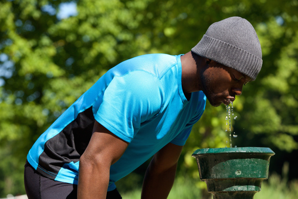 Νέο μαύρο άνθρωπος πόσιμο νερό από μια πηγή νερού - Φωτογραφία, εικόνα