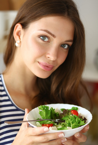 Νεαρή γυναίκα τρώει σαλάτα και κρατώντας μια ανάμικτη σαλάτα  - Φωτογραφία, εικόνα