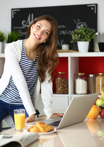 Attractive young woman using laptop and sitting in the kitchen  - Photo, Image