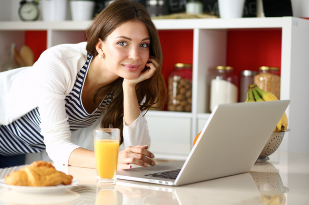 Attractive young woman using laptop and sitting in the kitchen  - Φωτογραφία, εικόνα