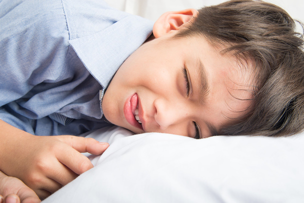 kleiner Junge legt sich auf das Bett niedlich schönes Gesicht auf weißem Hintergrund - Foto, Bild