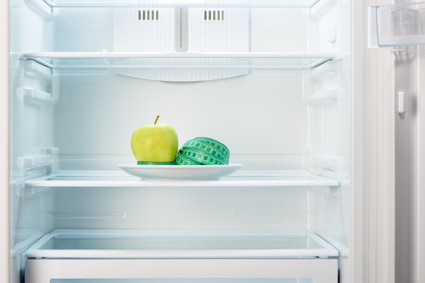 Apple with measuring tape on white plate in refrigerator - Zdjęcie, obraz