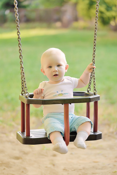 Happy baby boy having fun on a swing ride at a playground - Foto, Imagen