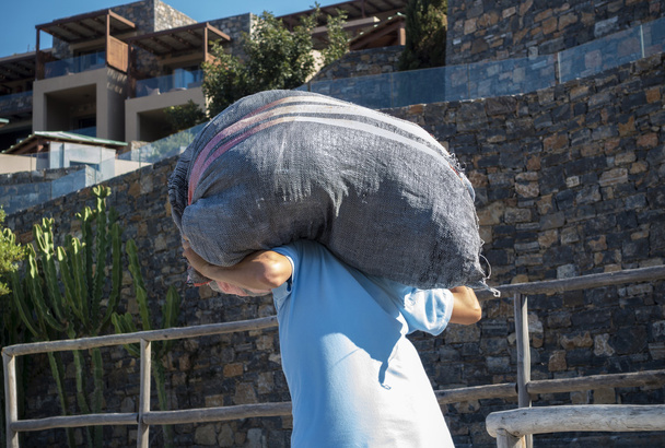 Εργαζόμενος φέρνει ένα τσουβάλι στην πλάτη του - Φωτογραφία, εικόνα