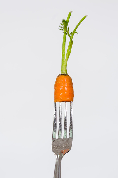 Closeup silver fork with small piece of organic carrot including stem and white background - Foto, Imagen