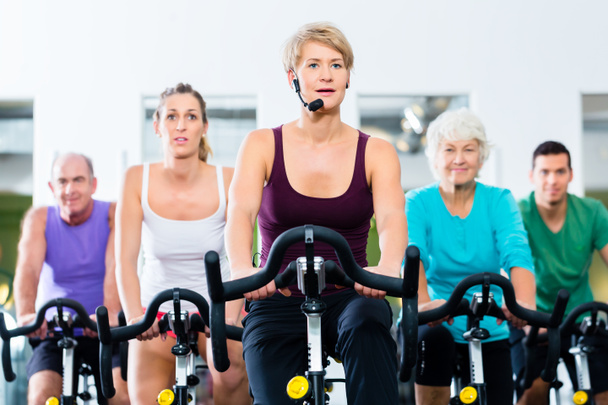 Senior mensen in sportschool spinnen op fitness fiets - Foto, afbeelding